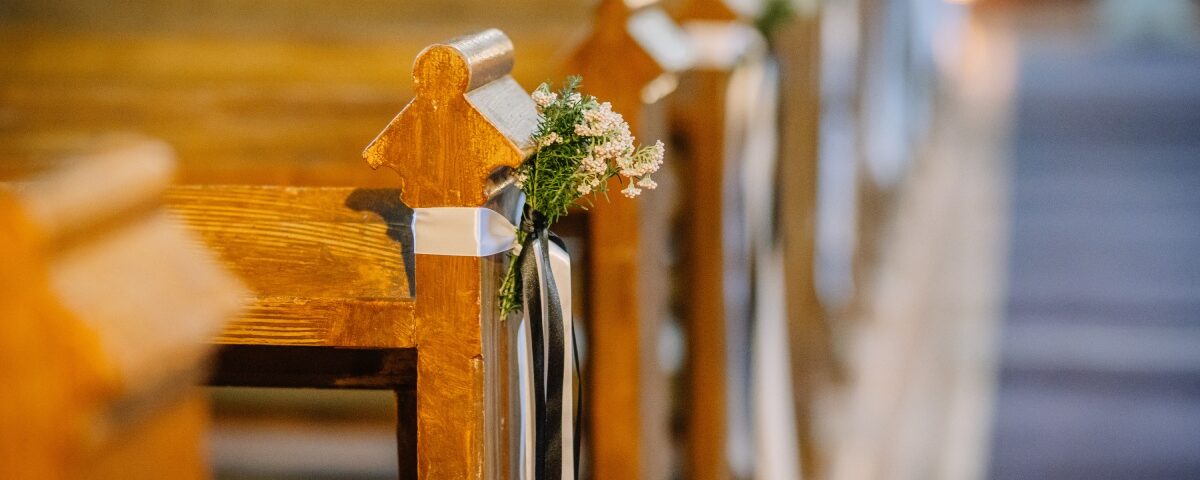Several wooden church pews have small bunches of flowers tied with white and black ribbons at each end.