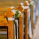 Several wooden church pews have small bunches of flowers tied with white and black ribbons at each end.