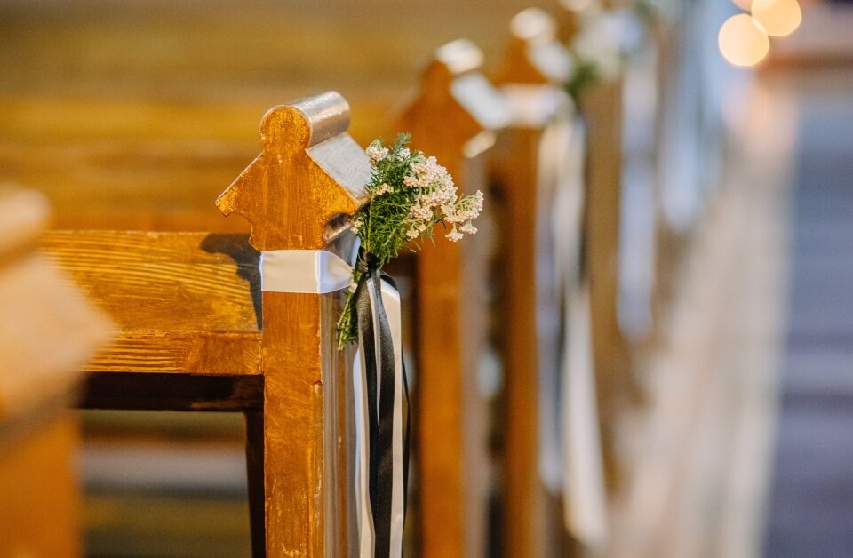 Several wooden church pews have small bunches of flowers tied with white and black ribbons at each end.
